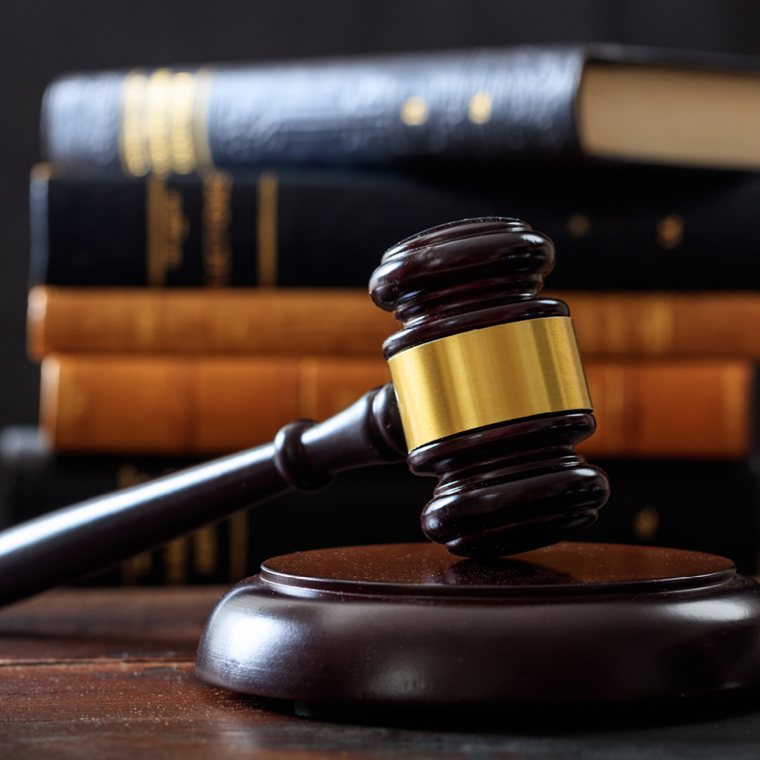 A wooden judge's gavel resting on its sound block with a stack of law books blurred in the background.