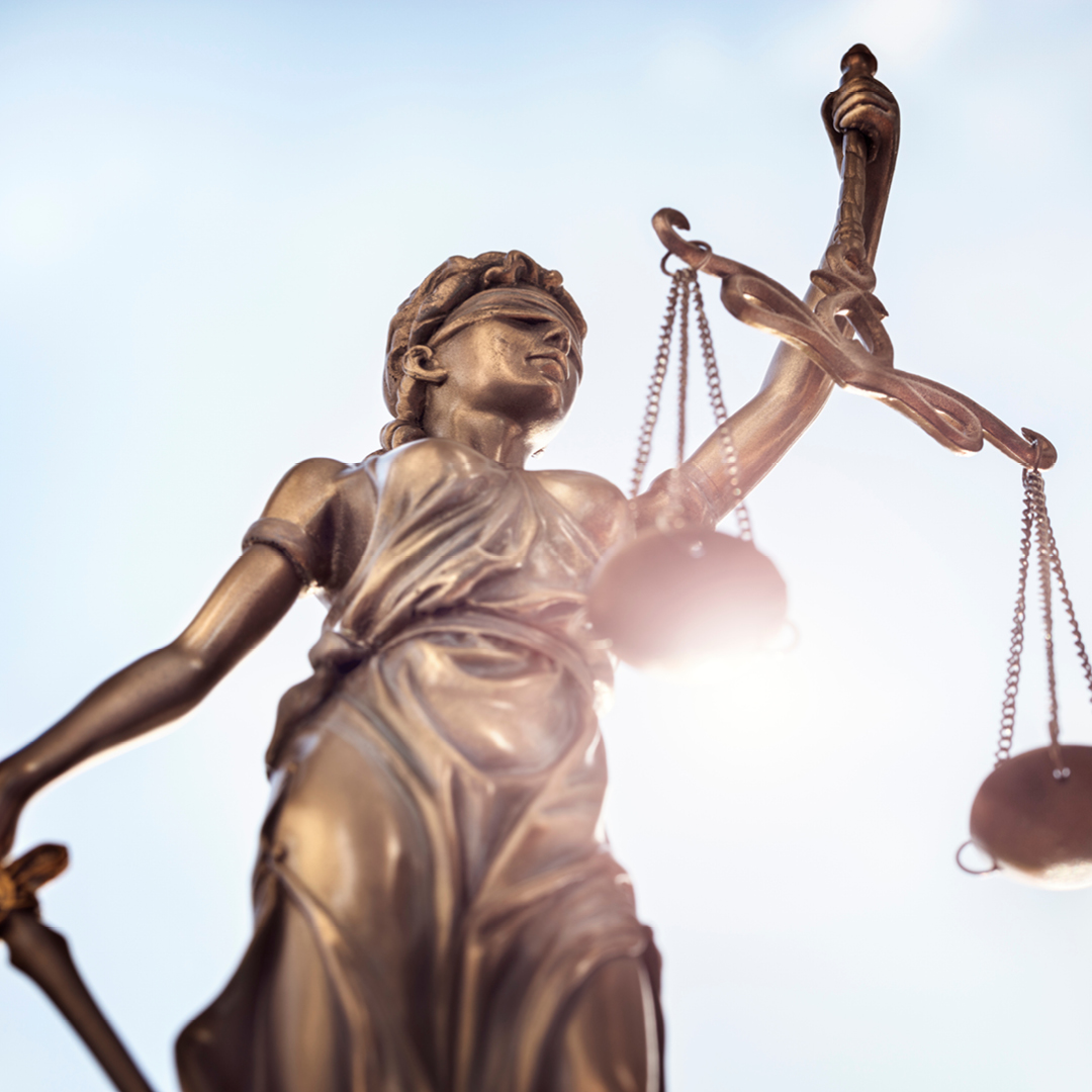 Statue of Lady Justice holding scales and a sword against a bright sky. The figure is blindfolded.