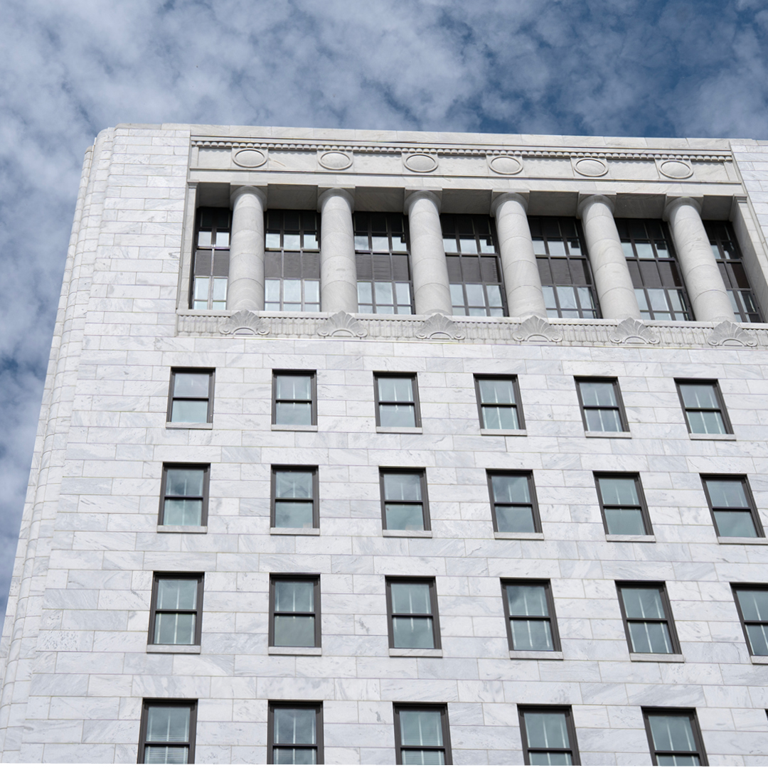 A low-angle, medium shot captures the light grey marble facade of the Ohio Judicial Center against a backdrop of blue sky filled with scattered white clouds.