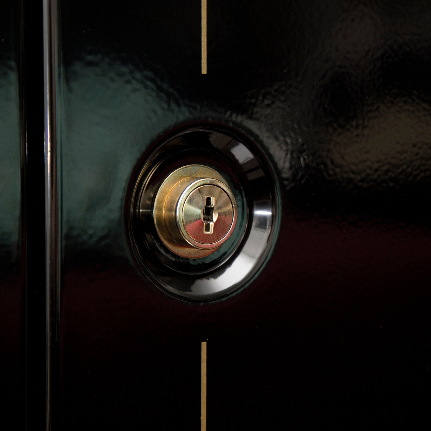 Close-up of a brass keyhole on a polished black surface, featuring a vertical gold line above it.