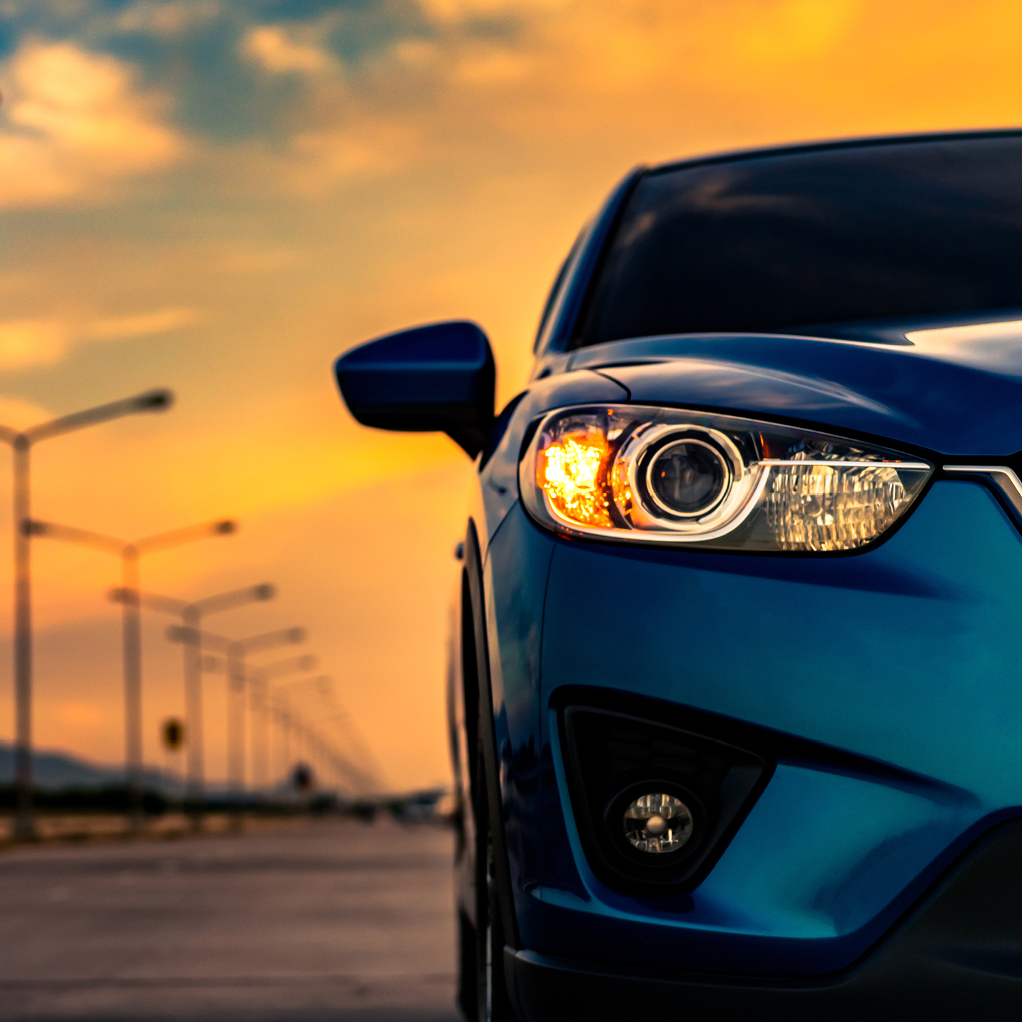 A blue car traveling along a road as the sun sets, casting warm colors across the sky.