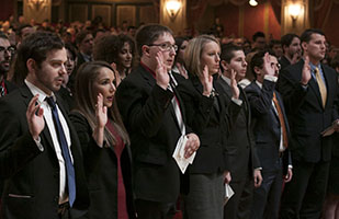 Image of men and women dressed in suits with their right hands raised taking the professional oath