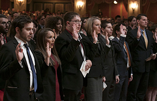 Image of people standing in an auditorium with their right hands raised while they are sworn in during a previous bar admissions ceremony