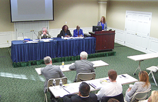 Image of people sitting on a discussion panel addressing an audience