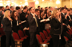 Image of men and women standing in an auditorium with their right hands raised