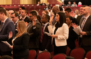 Image of an auditorium full of men and women raising their hands to take an oath