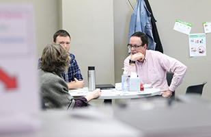 Image of two men and a woman sitting at a table talking