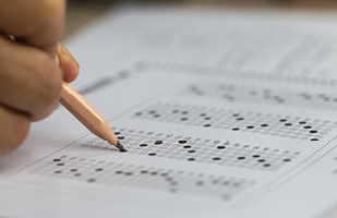 Image of someone filling in a bubble optical answer sheet with a pencil (smolaw11/iStock)