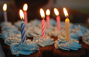 Image of several chocolate cupcakes, each containing a colored, lit candle