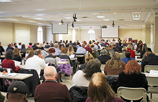 Image of the backs of dozens of people sitting in a seminar