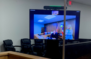 Image of a court proceeding displayed on a large monitor in a courtroom