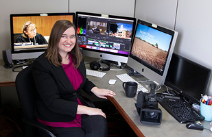 Image of a woman sitting at a desk in front of a row of monitors