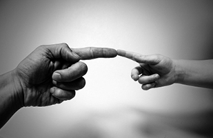 Image of an adult left hand on the left and a child's right hand on the right with their fore fingers touching end to end