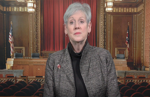 Image of a video screen of Chief Justice O'Connor with the Supreme Court Courtroom in the background