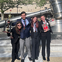 Image of two boys and two girls, all wearing suits, wearing medals, posing in front of the giant, stainless steel gavel in the south reflecting pool of the Thomas J. Moyer Ohio Judicial Center. One boy is holding a trophy, while a girl is holding a plaque and certificate.