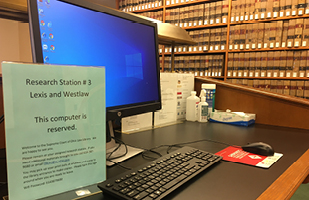 Image of a desk with a computer on it in the foreground and shelves of law books in the background