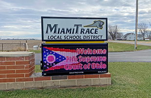 Image shows a sign that reads 'Miami Trace Local School District' above an electronic LED sign tht has the Ohio flag and the words 'Welcome The Surpreme Court of Ohio'