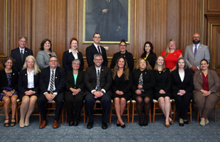 A group of people in suits and professional attire sitting for a photo in front of portraits.