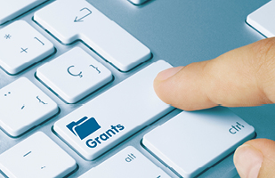 Image of someone's index finger pushing a button on a computer keyboard that says 'Grants' below a folder icon