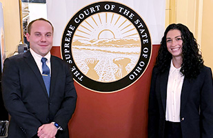 A smiling man and a woman stand next to a graphic showing the seal of the Supreme Court of Ohio