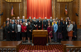 Three rows of men and women posing for a photo in the courtroom of the Thomas J. Moyer Ohio Judicial Center.