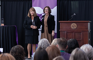 Two women standing by a wooden podium, one is holding a clear, acrylic award.