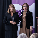 Two women standing by a wooden podium, one is holding a clear, acrylic award.