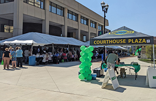 A row of canopied booths set up along the side of a multi-story building in a parking lot.