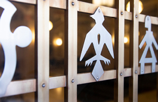 Close-up of a bronze door decorated with silver cutouts in the shape of a bird and a person.