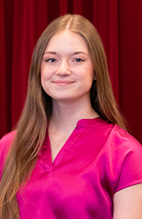 Image of a young woman with long, auburn hair wearing a pink, short-sleeve blouse.