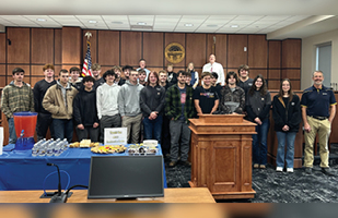 Several rows of high school students and court staff pose for a picture in a courtroom.