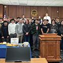 Several rows of high school students and court staff pose for a picture in a courtroom.