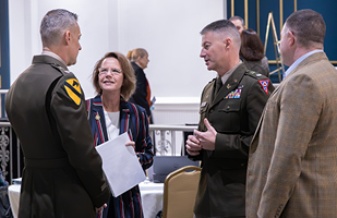 A woman wearing a red, white, and blue stiped blazer stands between to men wearing military dress uniforms.