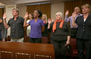 Image showing two rows of men and women standing in a jury box and holding their right hands up as if taking an oath.