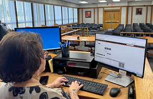 A woman typing on a computer at a desk in a room full of chairs