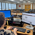 A woman typing on a computer at a desk in a room full of chairs