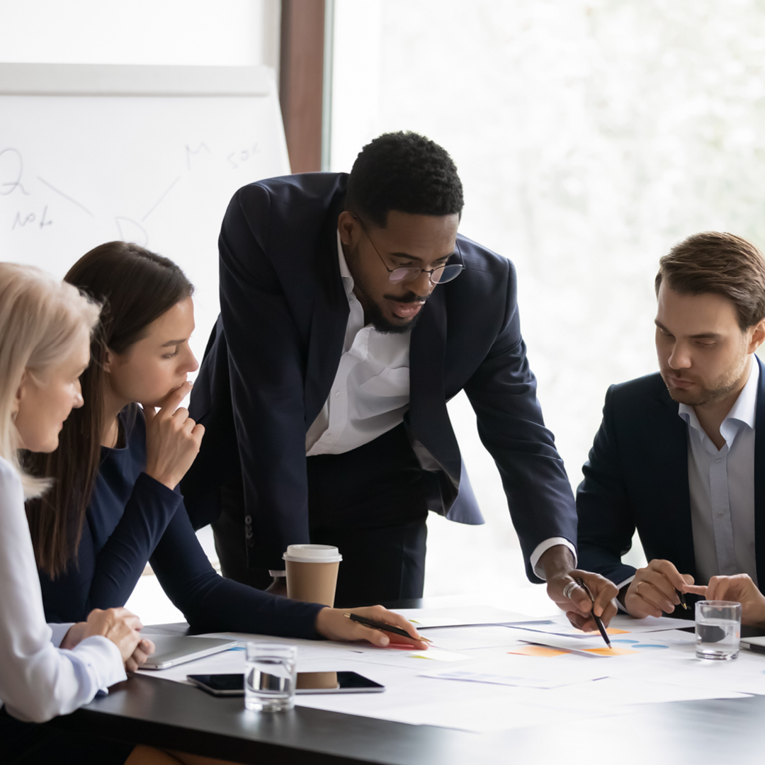Two women and two men seated at a table discussing documents placed on the table.