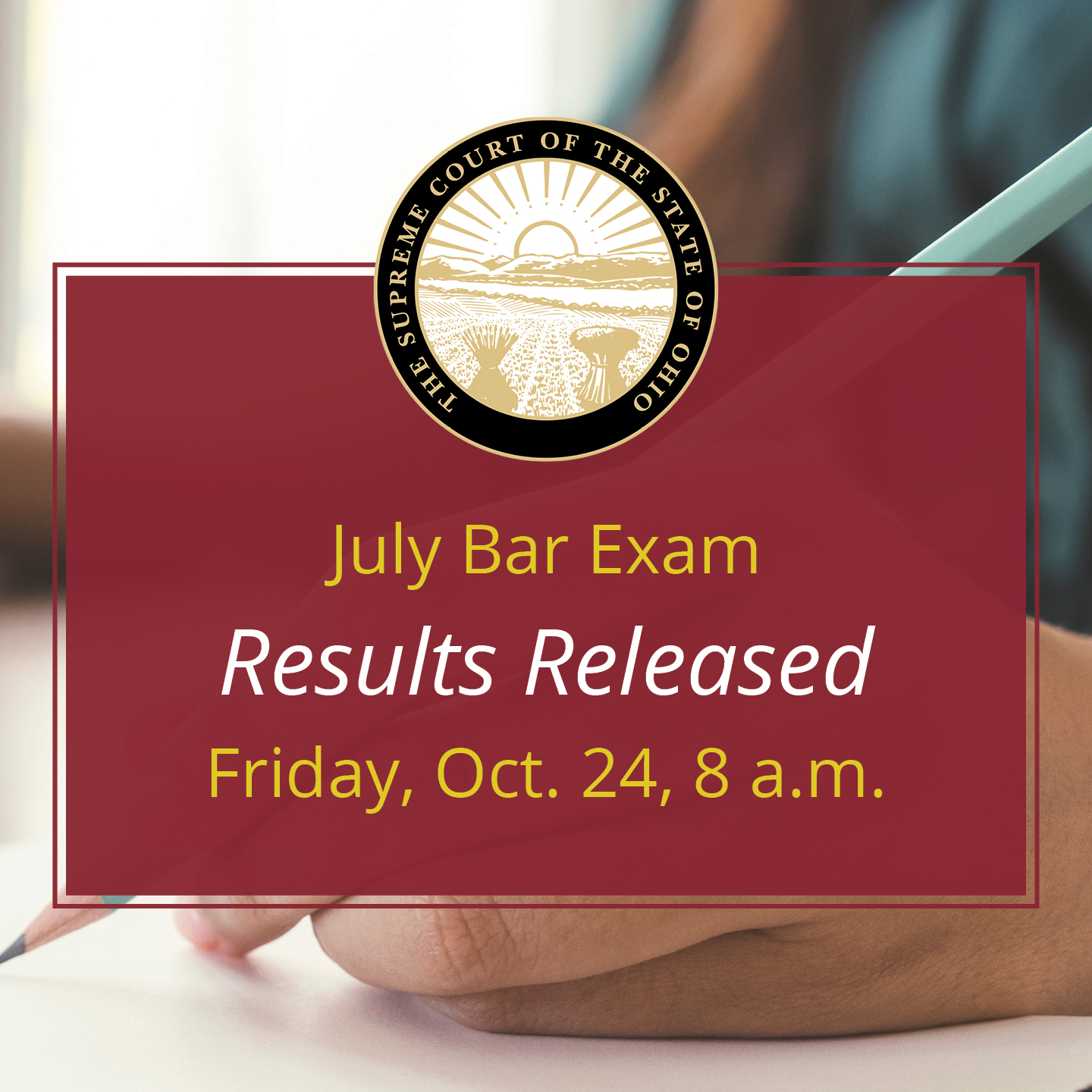 A hand up close writing on paper with text that reads 'July Bar Exam Reults Released Friday, Oct. 24, 8a.m.'