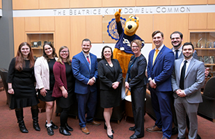 A group of nine men and women posing in front of the University of Akron mascot, Zippy.