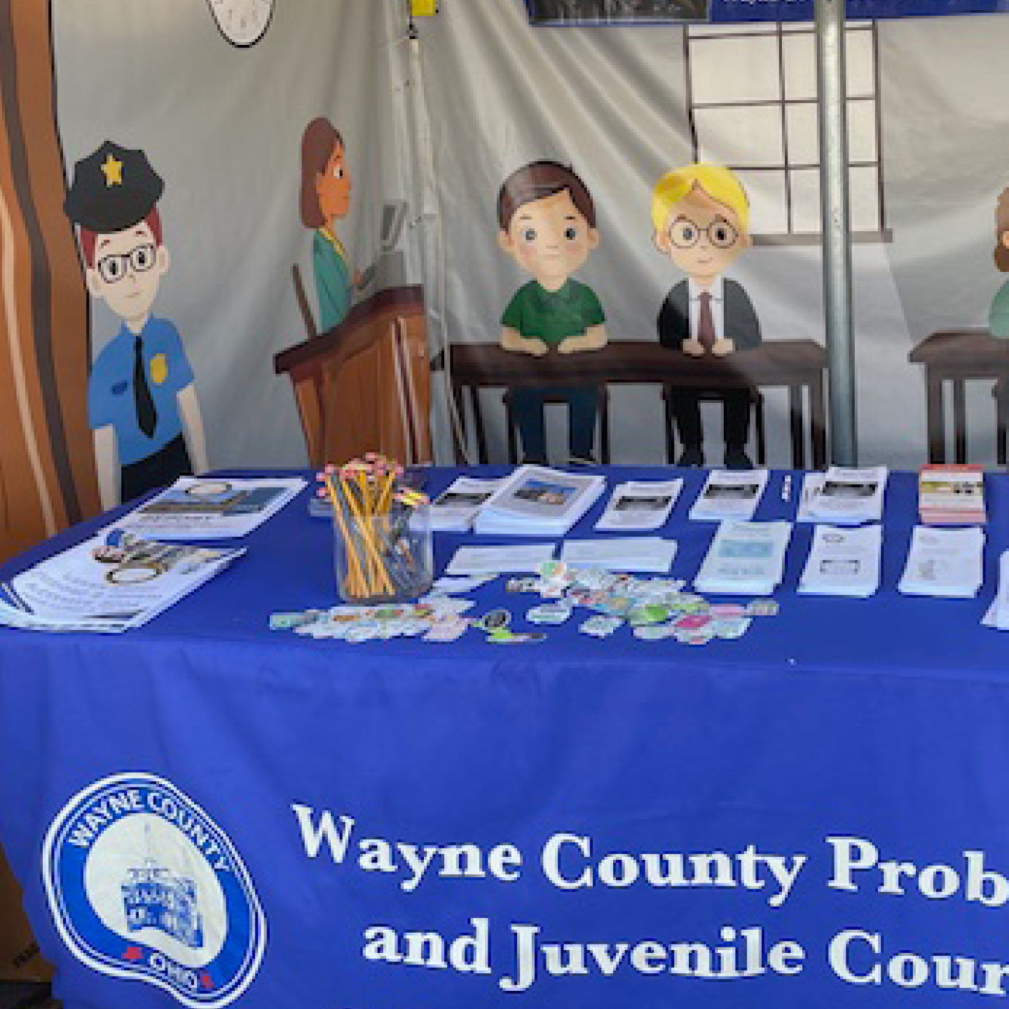 A table in a tent with informational handouts, pencils, and stickers with a courtroom theme