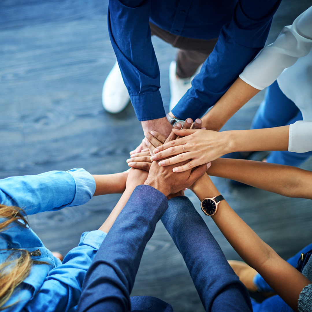 A group standing in a circle with their hands stacked on each other