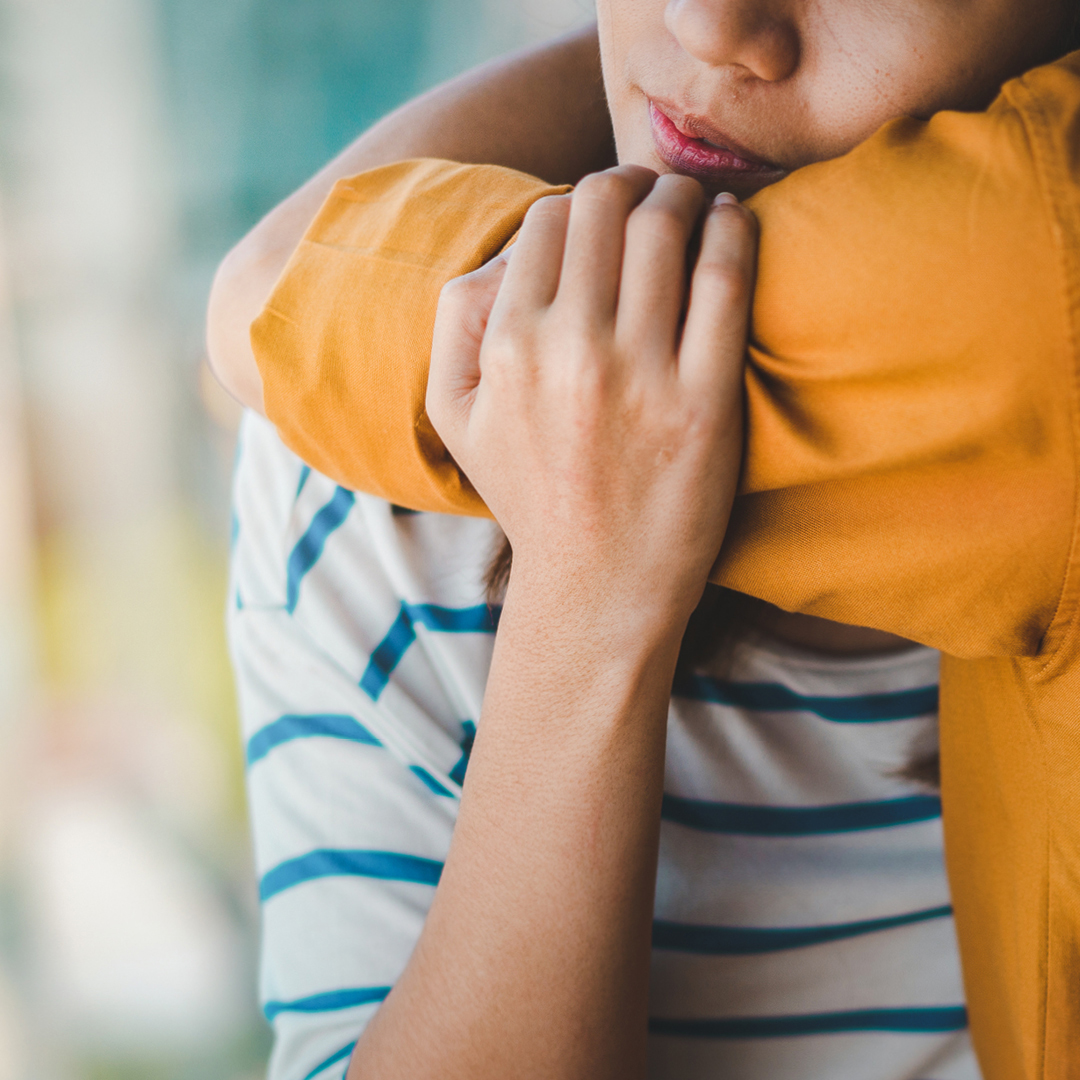A woman wearing a teal blue and white striped shirt embracing a boy in a yellow shirt
