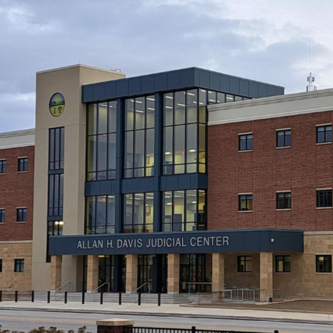A group of men and women wearing winter coats standing outside listening to a woman speak with a booklet