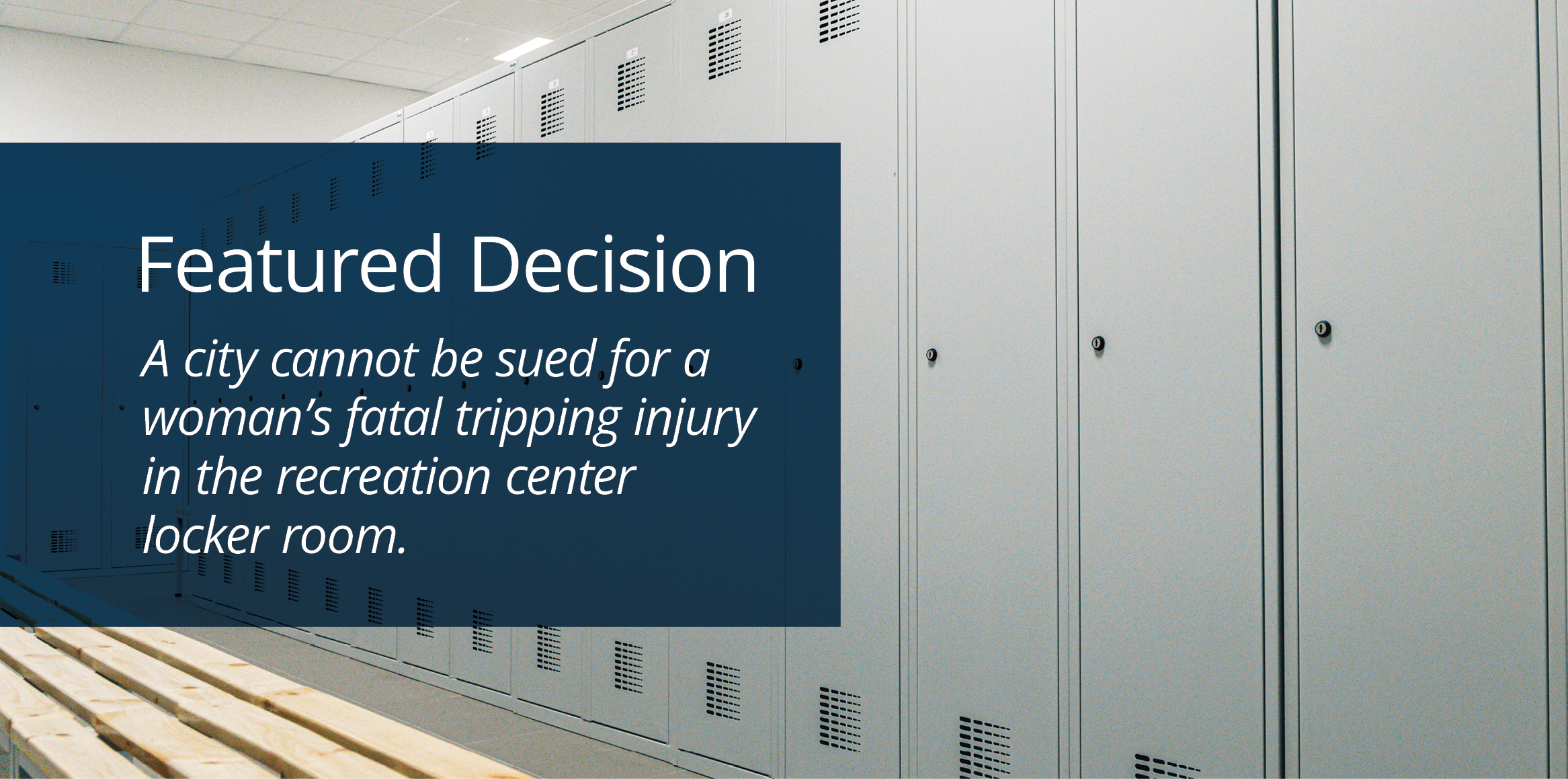 A long row of tall, light gray metal lockers lining a locker room wall next to a wooden bench.