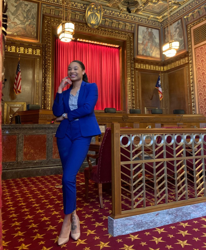 Image of a smiling woman wearing a blue suit standing in the courtroom of the Thomas J. Moyer Ohio Judicial Center