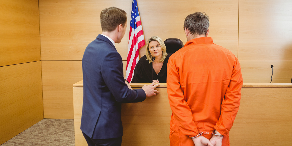 Image containing an attorney and a man wearing an orange prison jumpsuit standing before a judge in a courtroom
