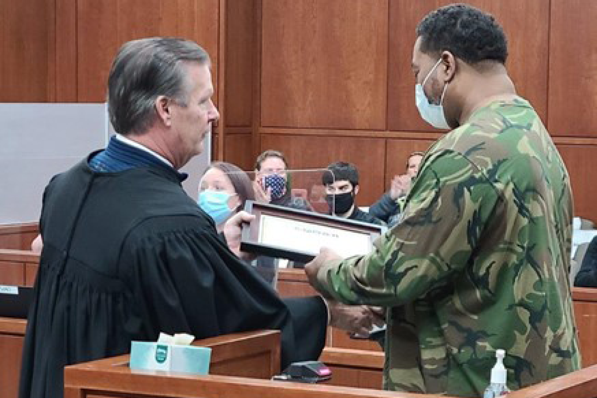 Image of a judge wearing his judicial robe handing a framed diploma to man wearing a camoflage shirt
