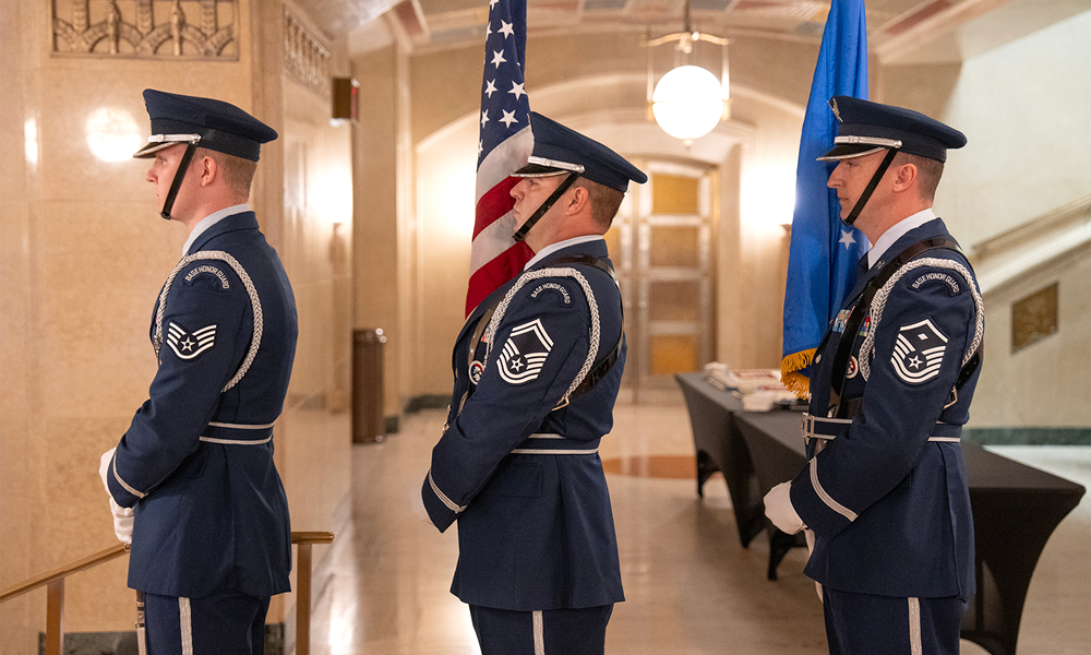 Three men wearing Air Force honor guard uniforms stand in line preparing to descend a staircase.