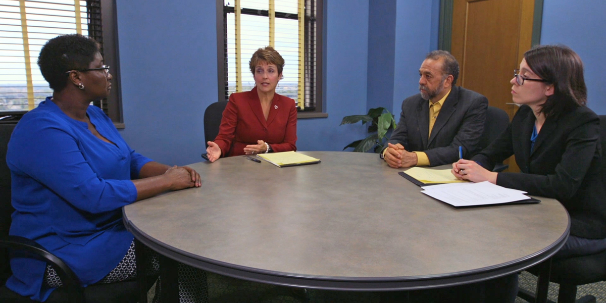 Three women and one man seated at a round table in a room with blue walls.