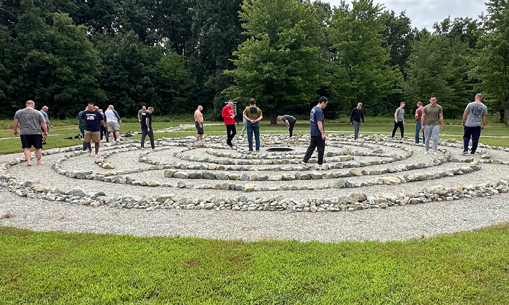 A group of men walk a circular labrynth constructed with rocks.
